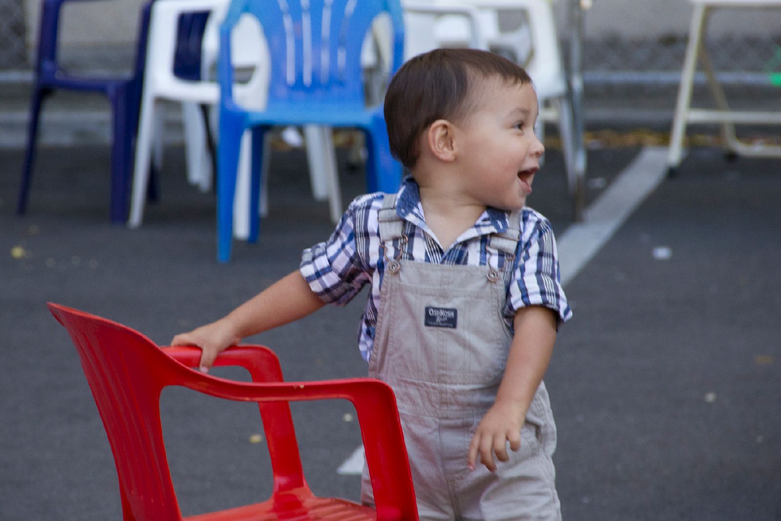 A toddler in overalls looks behind him excitedly.